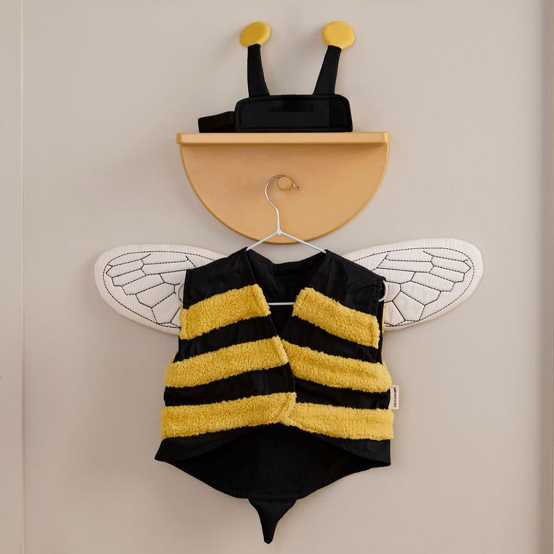 Kids Concept verkleedkleding hommel hangt aan een haakje aan de muur, met het gestreepte vest en de vleugels naar voren.