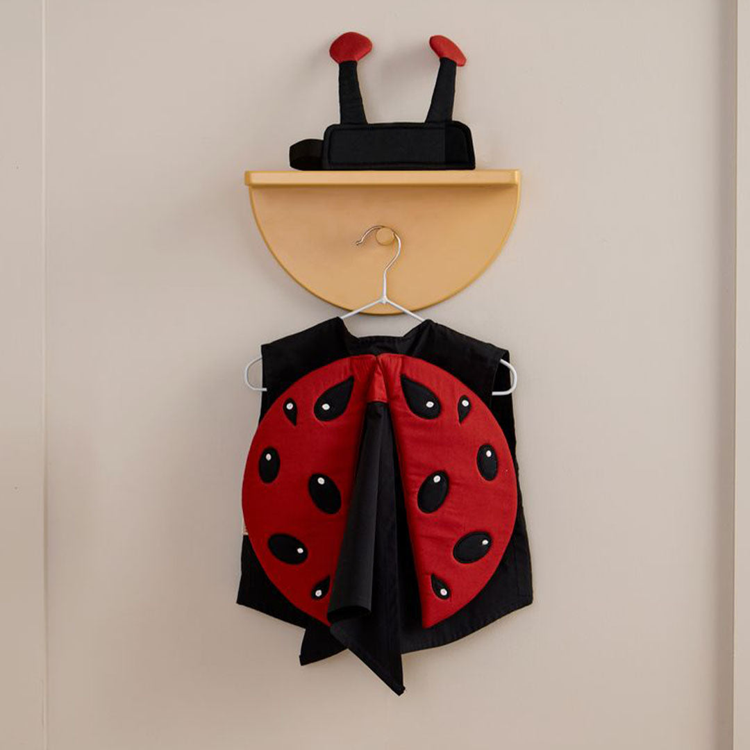 Het lieveheersbeestje kinderkostuum hangt aan een hanger aan de muur, met de hoofdband erboven op een plank.
