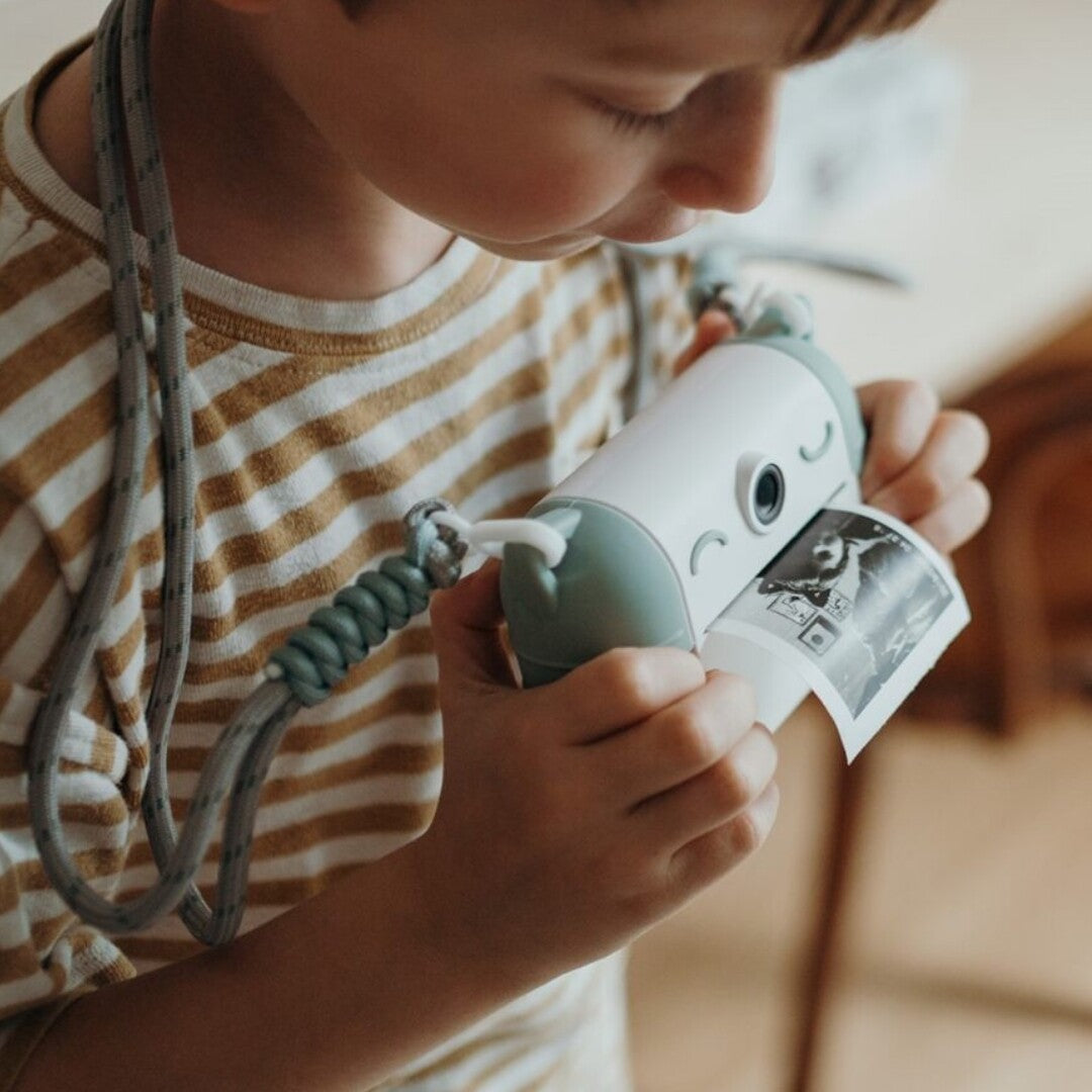 Een kind houdt een lichtblauwe kidywolf kindercamera vast en kijkt naar een zojuist geprinte foto.