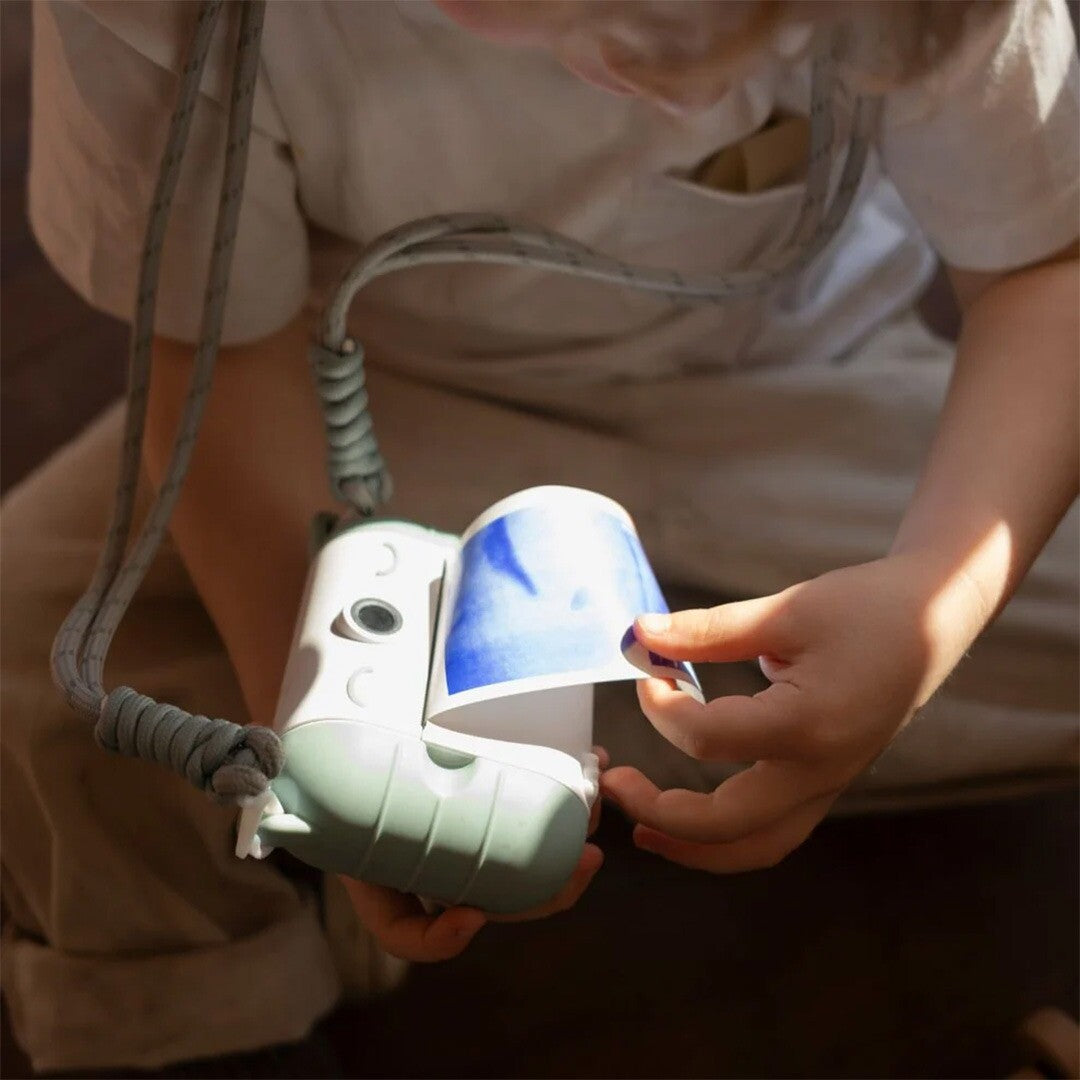 Kinderhanden trekken een blauwgekleurde foto uit een Kidyprint kindercamera.