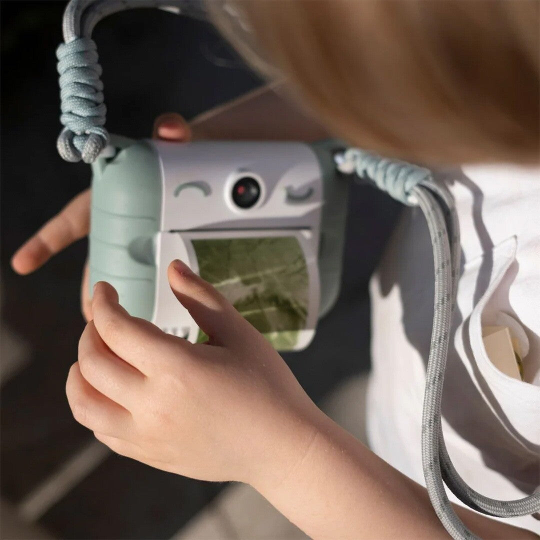 Kinderhanden houden een Kidyprint kindercamera vast waar een groen gekleurde foto uitkomt.