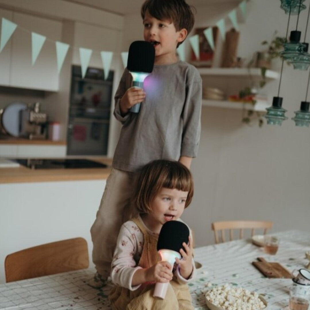 Twee kinderen zingen met oplichtende Kidywolf roze karaoke microfoons aan een tafel.