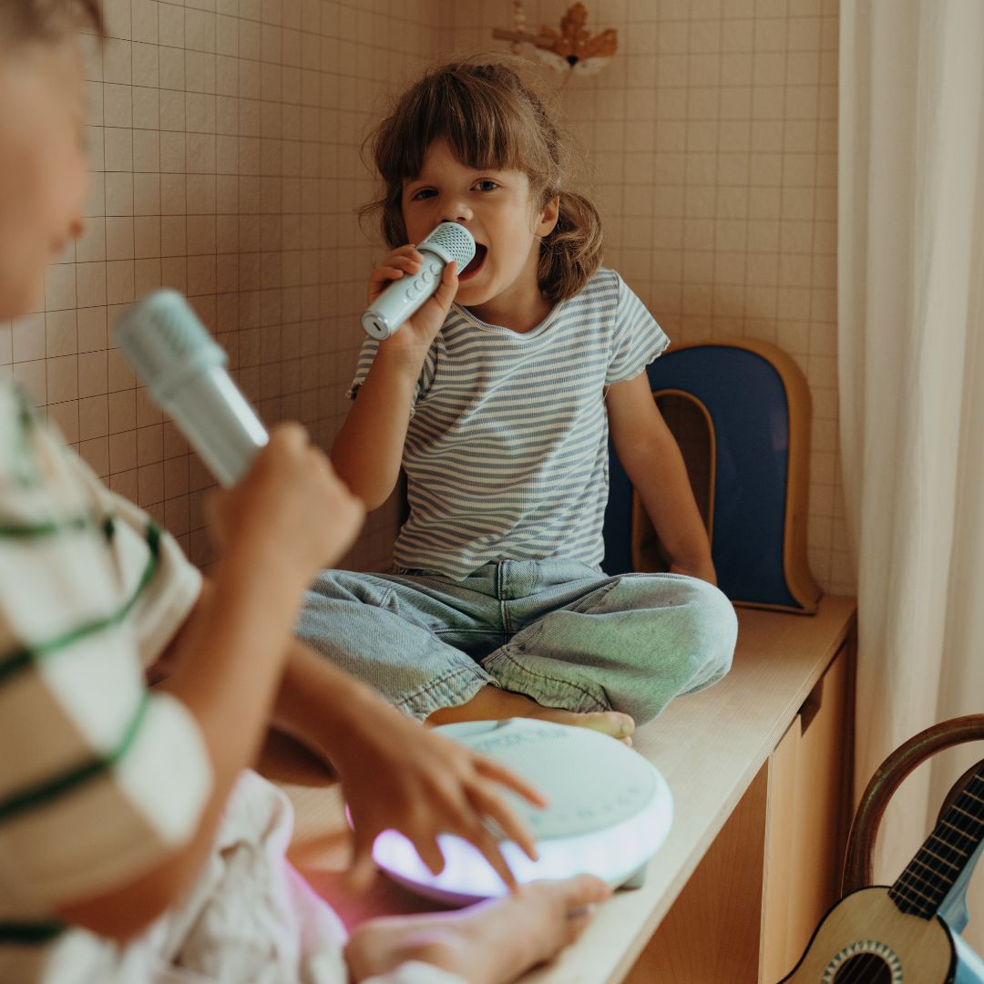 Twee kinderen spelen met de Kidywolf karaokeset, waarbij een meisje in een microfoon zingt.