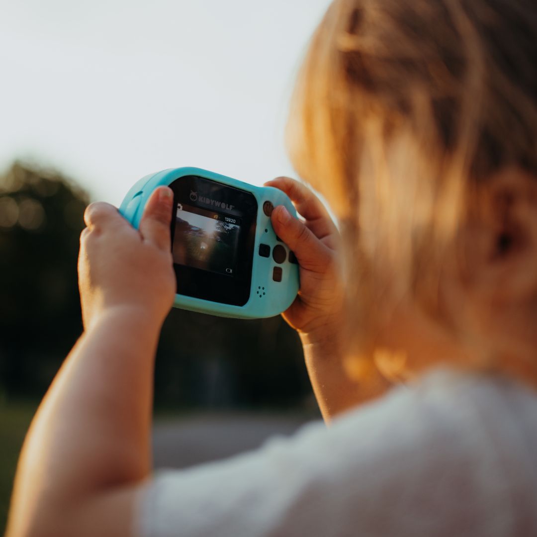 Een kind maakt een foto met de cyaan Kidywolf kindercamera kidycam, gezien over de schouder.