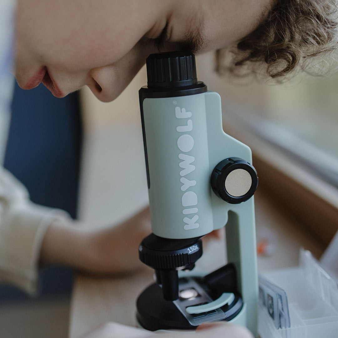 Een kind kijkt van dichtbij door het oculair van de Kidywolf educatieve microscoop.