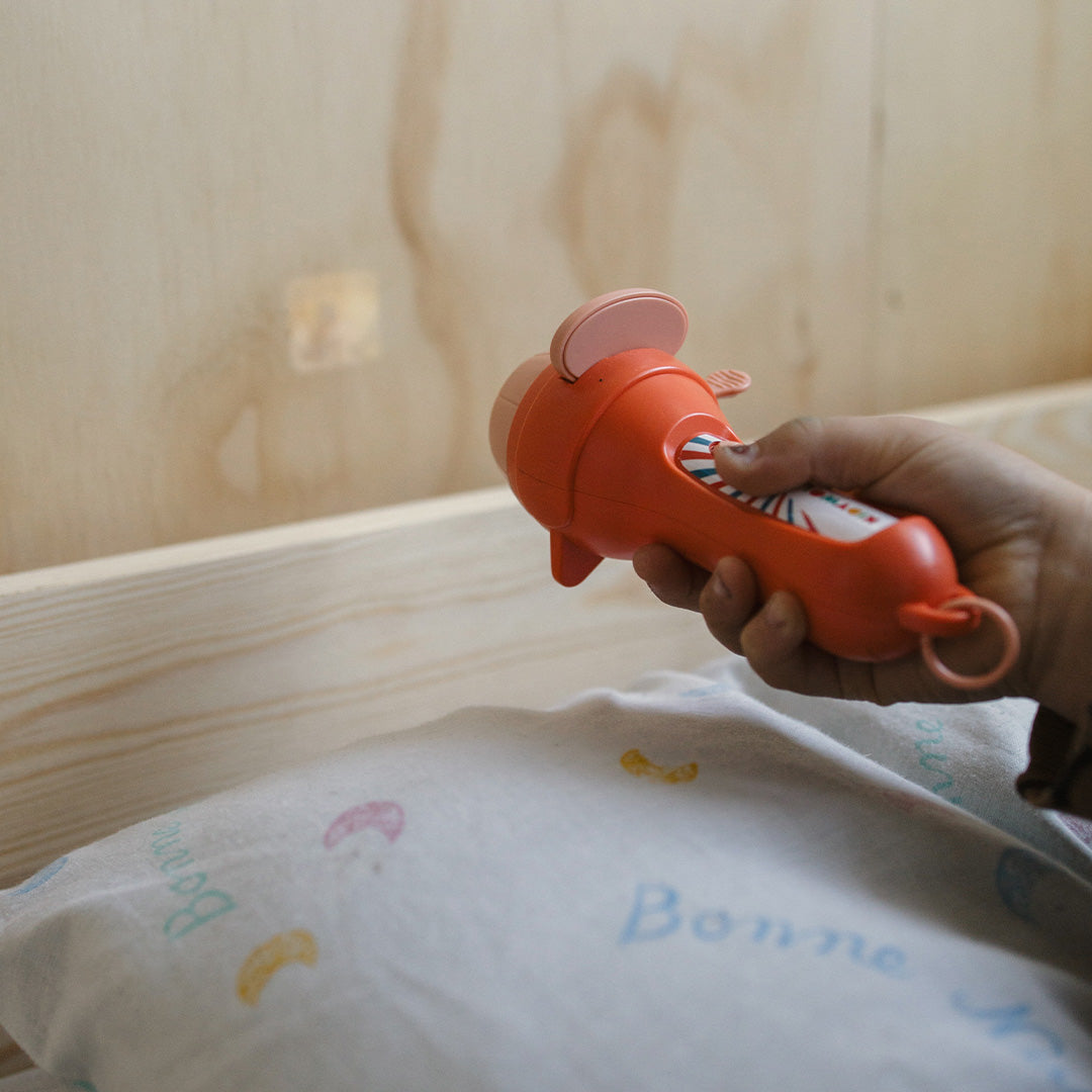 Een kinderhand houdt de Kidywolf oranje projector zaklamp boven een deken.