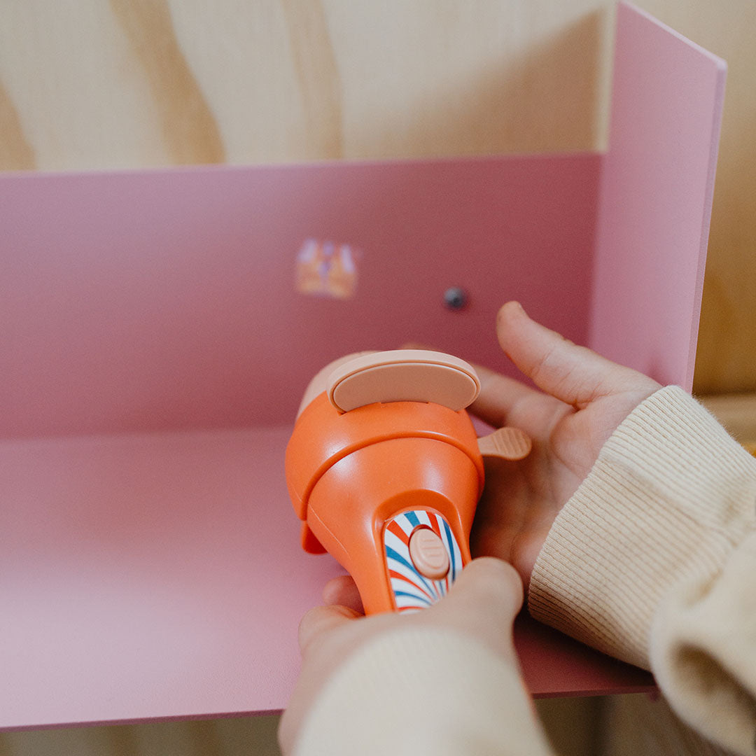 Een Kidywolf oranje projector zaklamp projecteert een afbeelding op een roze oppervlak.