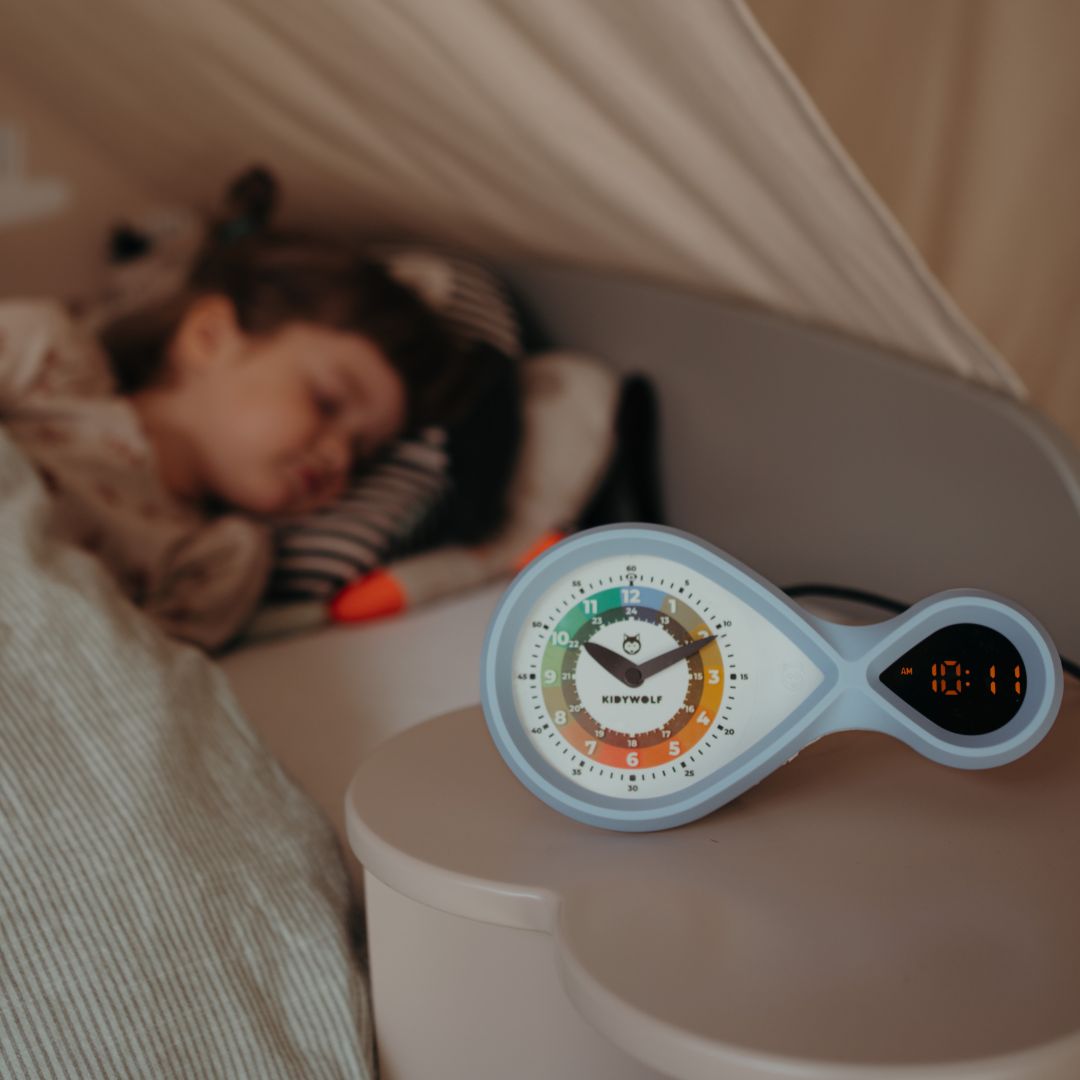Kidywolf educatieve wekker op een nachtkastje naast een slapend kind.
