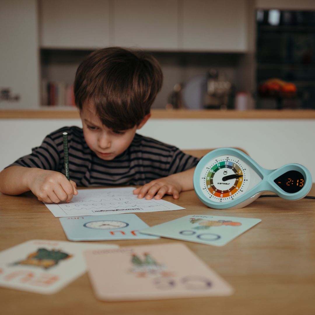 Een kind zit aan tafel te schrijven met de Kidywolf educatieve wekker ernaast.