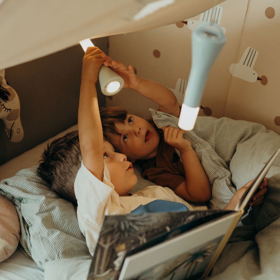 Twee kinderen liggen in bed onder een deken en schijnen met Kidywolf blauwe zaklampen.