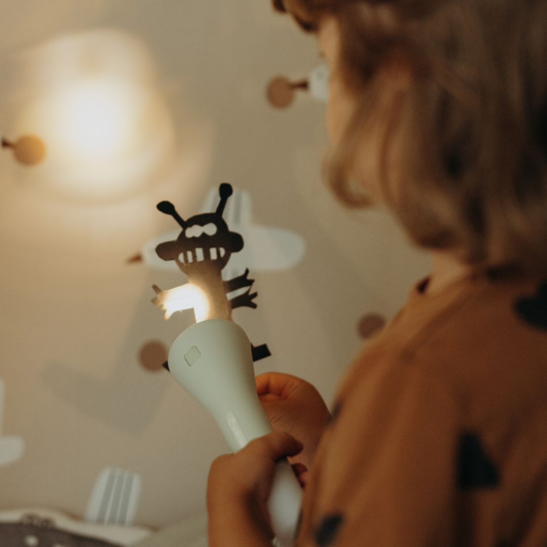Een kind projecteert een schaduwmonster op de muur met een groene zaklamp.