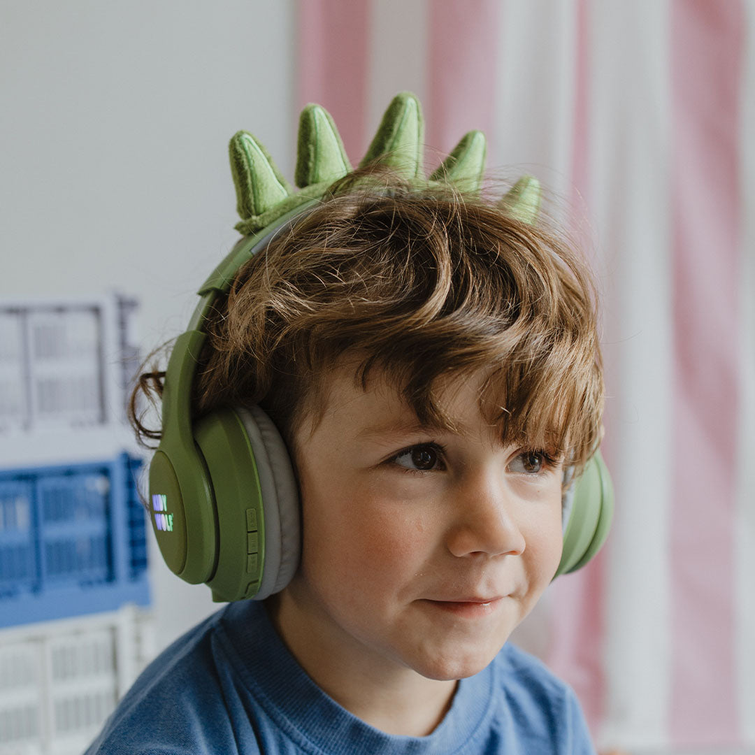 Een jongen draagt de groene Kidywolf kinderkoptelefoon met dinosaurus-spikes.