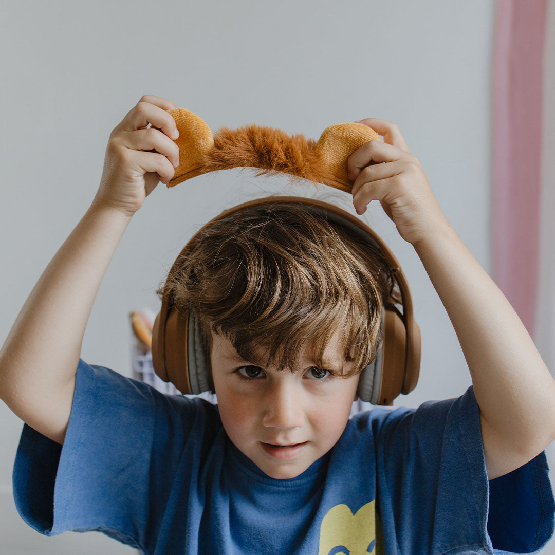 Een jongen draagt de bruine kinderkoptelefoon en houdt de leeuwenoren hoofdband boven zijn hoofd.