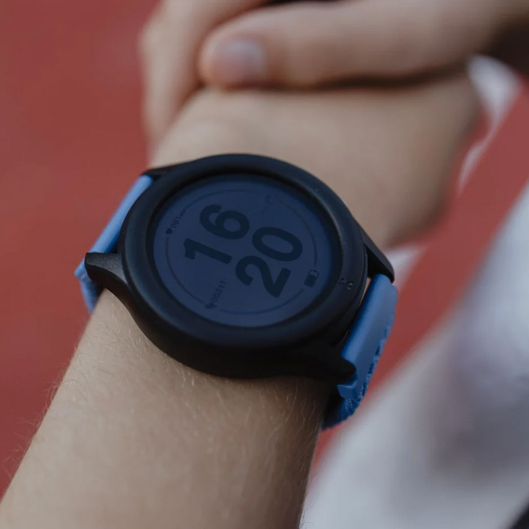 Close-up van de Kidywolf K-Watch om een kinderpols, met een donkerblauw digitaal scherm.