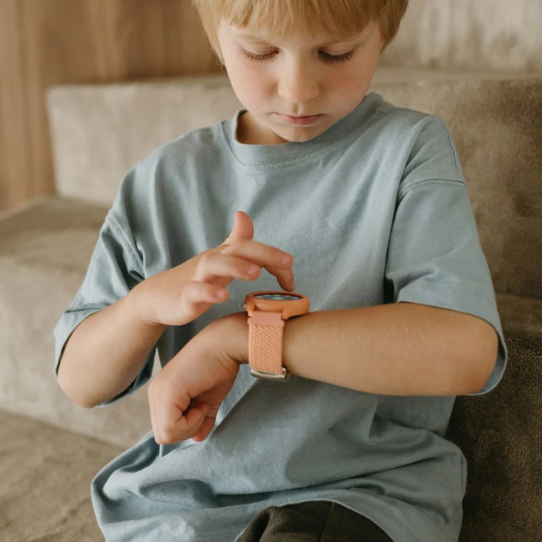 Een jongen kijkt naar en tikt op het Kidywolf K-Watch interactief horloge in koraal kleur om zijn pols.