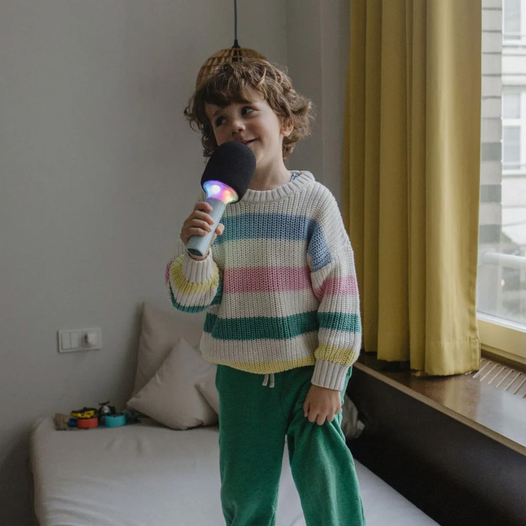 Een lachend kind zingt in de Kidywolf karaoke microfoon met gekleurde verlichting.