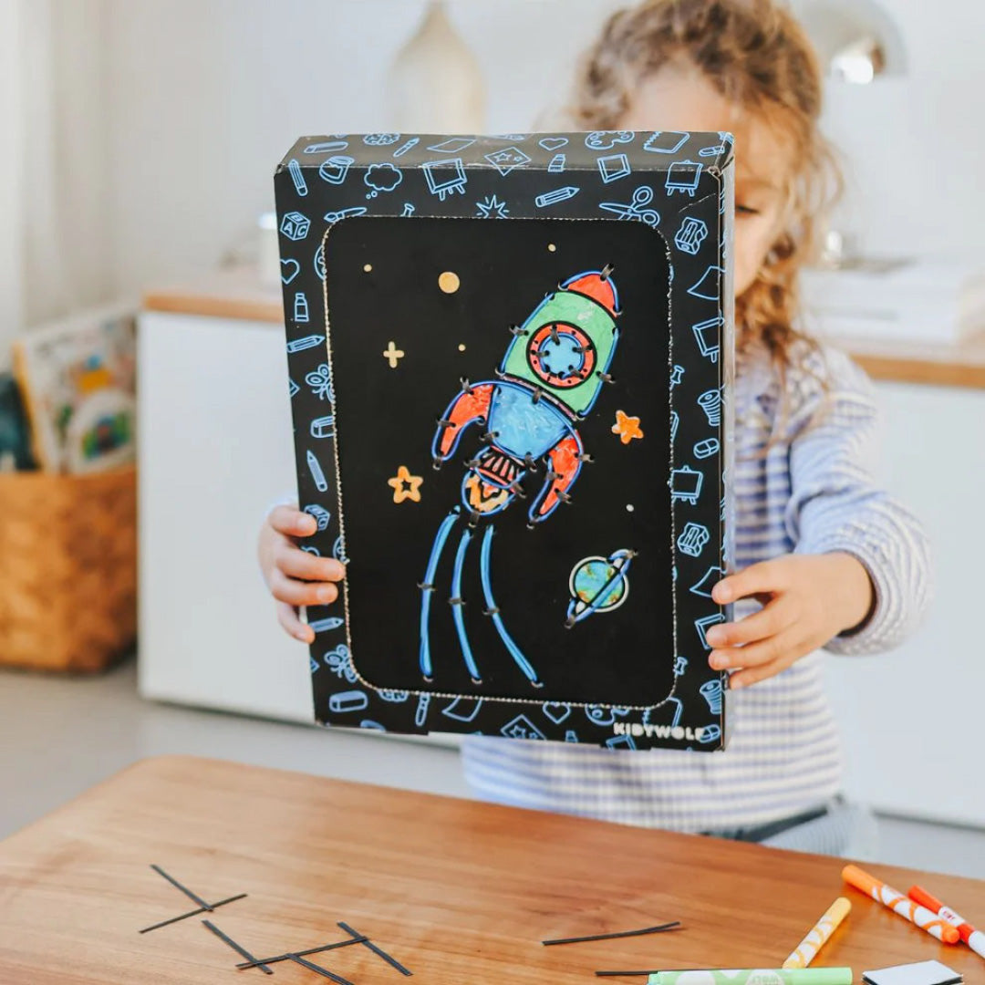 Een kind houdt een afgewerkte Kidywolf Kidyneon wanddecoratie met een kleurrijke raket vast.