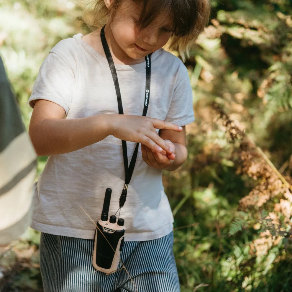 Een kind staat buiten met een roze kidywolf Kidytalk walkie talkie om de nek, hangend aan een draagkoord.