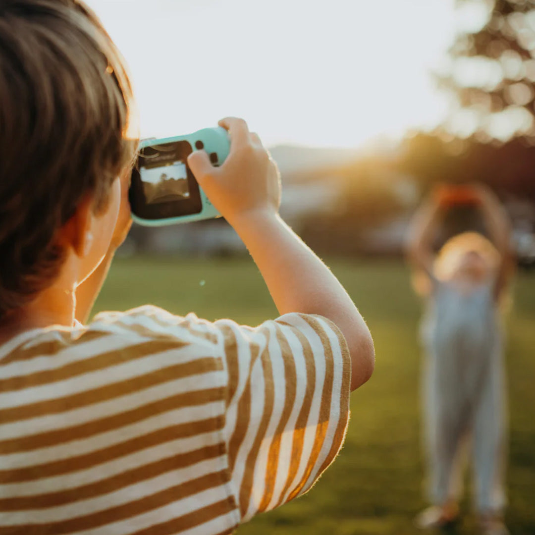 Een kind fotografeert een ander kind met de cyaan Kidywolf kindercamera kidycam, gezien over de schouder.