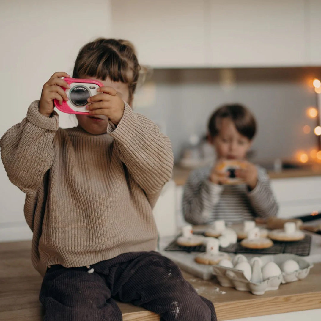 Een kind maakt een foto met een roze kindercamera in een keuken.