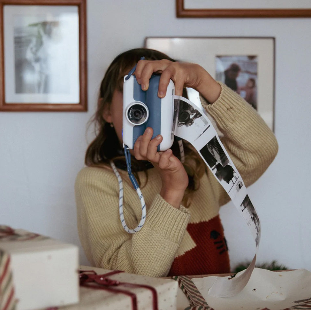 Een kind gebruikt de Kidywolf kindercamera om een foto te maken, met een lange strook zwart-witfoto's die eruit komt.
