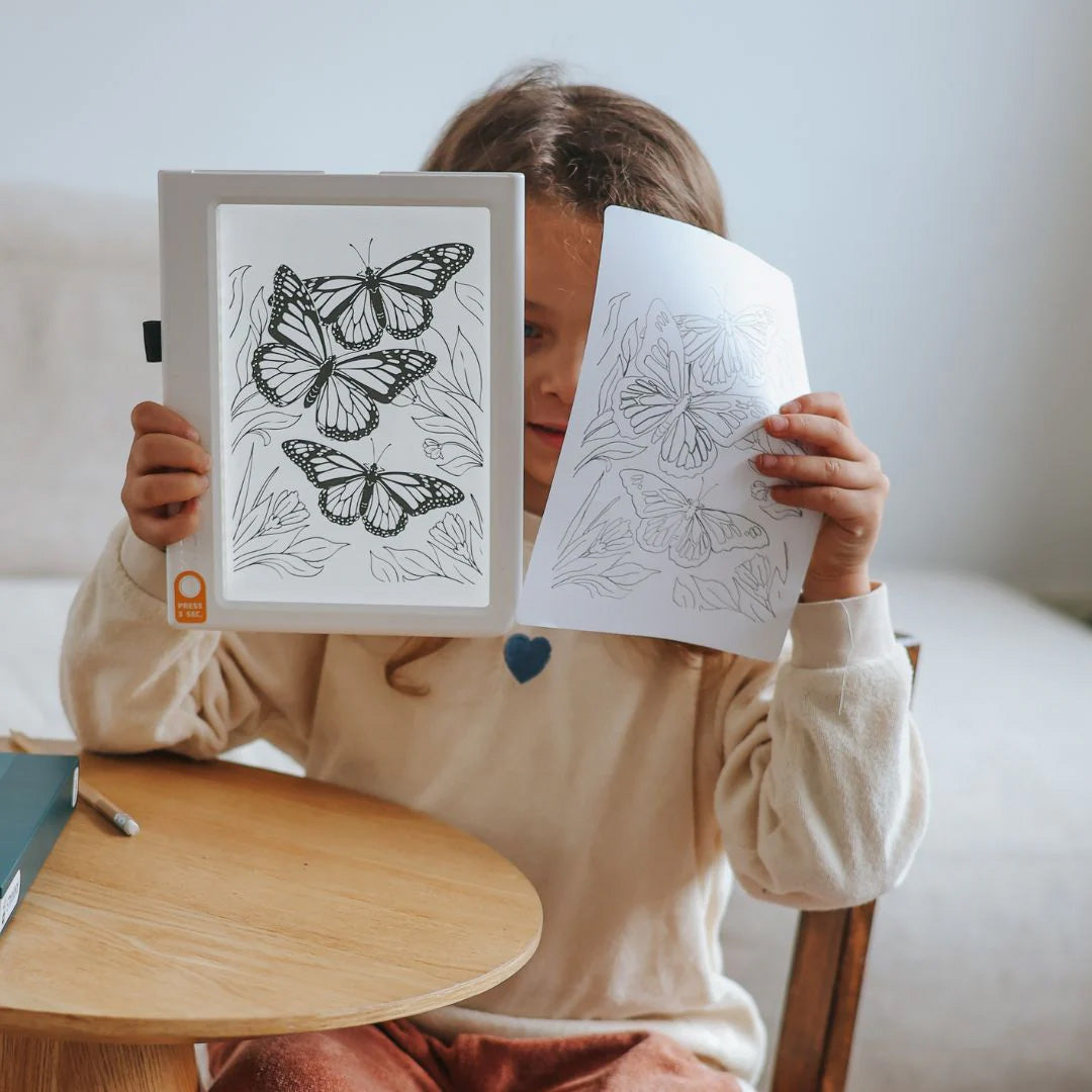 Een kind houdt het Kidywolf KidyDraw tekenbord met een vlindertekening en een losse schets van vlinders omhoog.