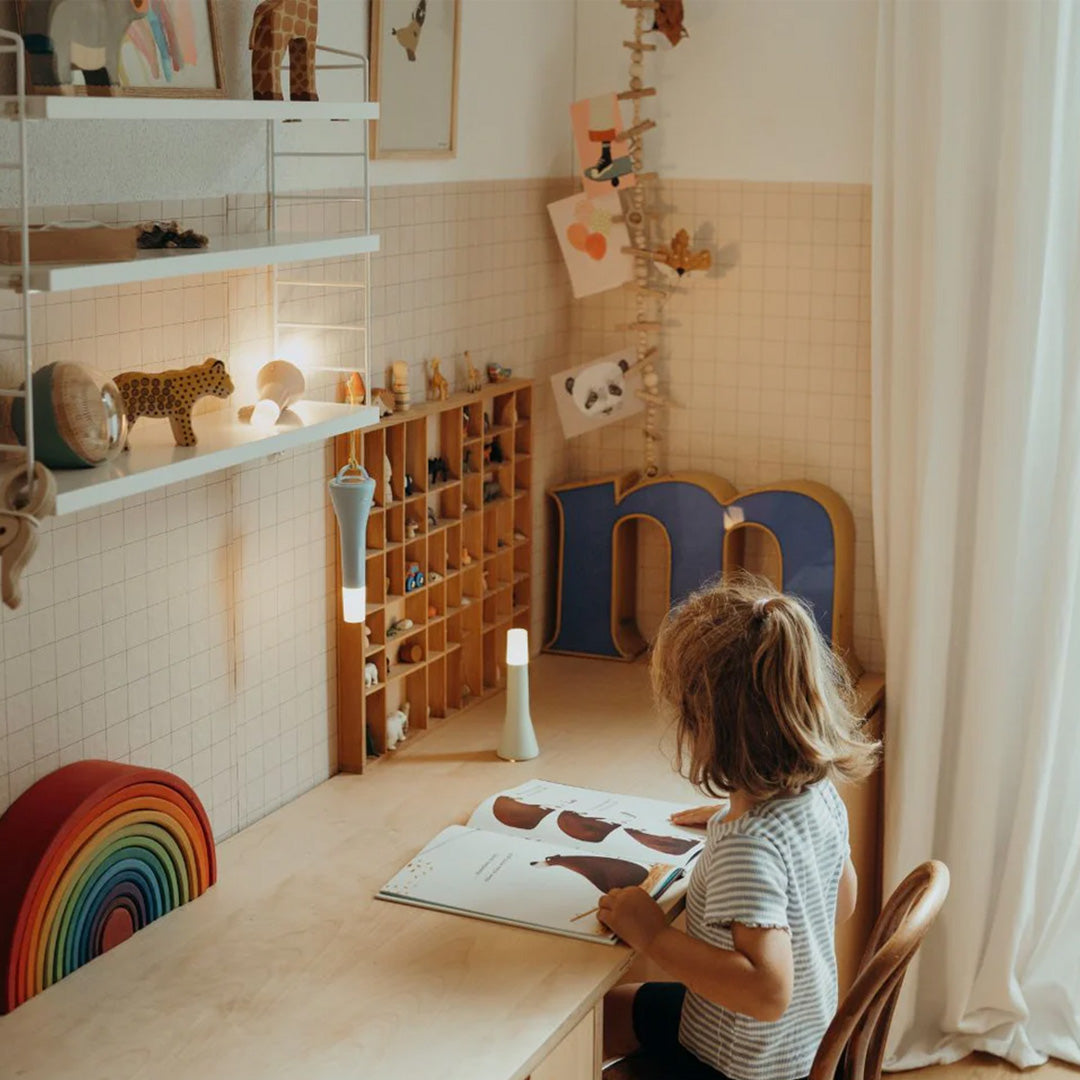 Een kind zit aan een houten bureau en leest een boek, met twee Kidywolf blauwe zaklampen op het bureau.