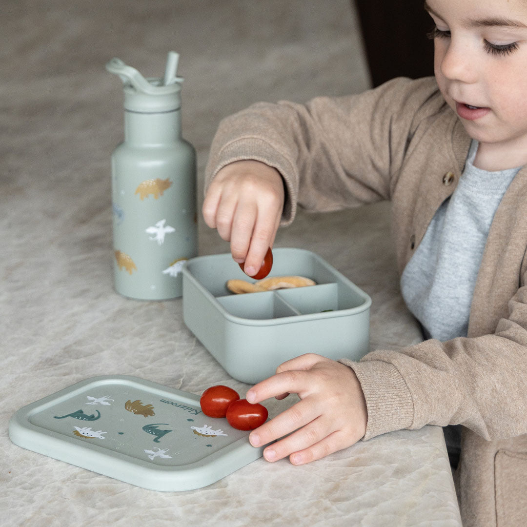 Een kind vult een Kidzroom broodtrommel met vakjes en dinosaurusdeksel met cherrytomaten.