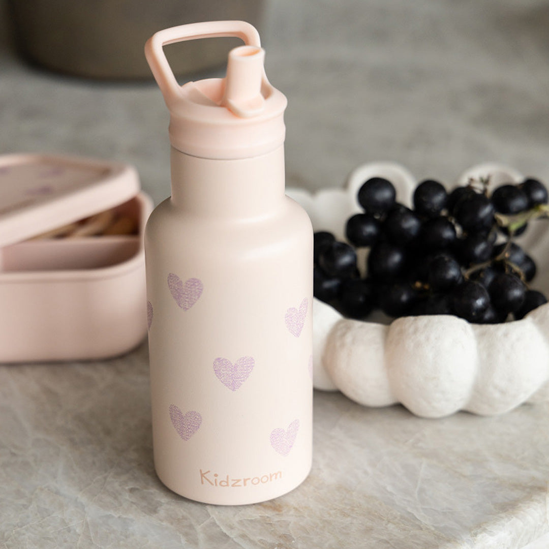 Kidzroom roze RVS drinkfles met glitterharten op een marmeren tafel naast een schaal druiven.