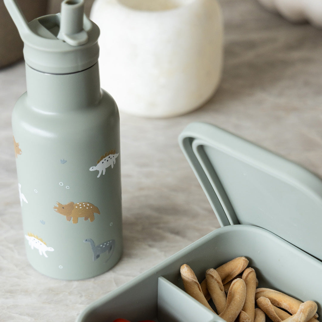 Kidzroom groene drinkfles met dinosauruspatroon naast een open lunchbox met snacks.