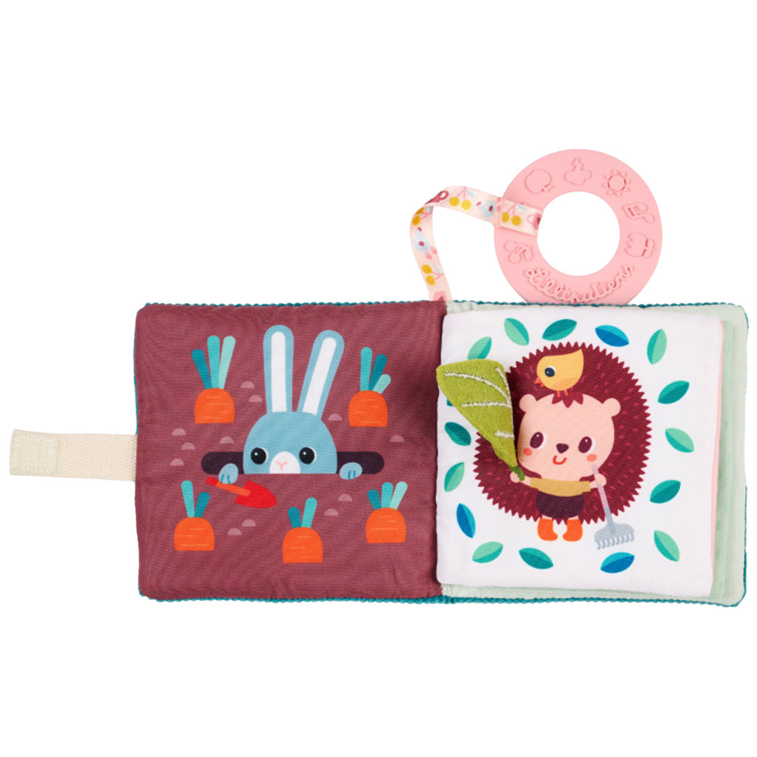 Open Lilliputiens activiteitenboek voor baby's met een konijn tussen wortels en een egel met hark, inclusief roze bijtring.