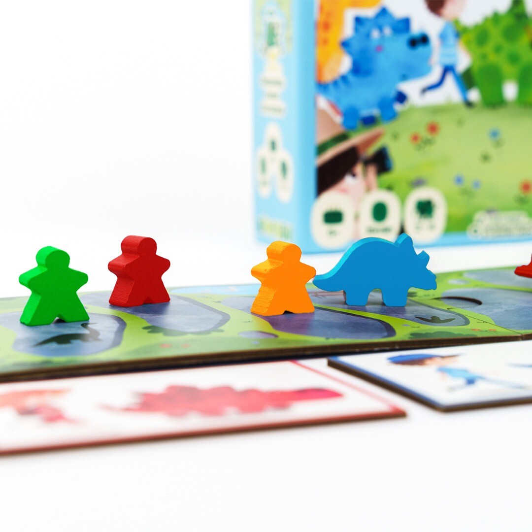 Detail van het Kiwizou BalaDino bordspel met houten speelfiguren, waaronder een blauwe dinosaurus en drie menselijke pionnen.