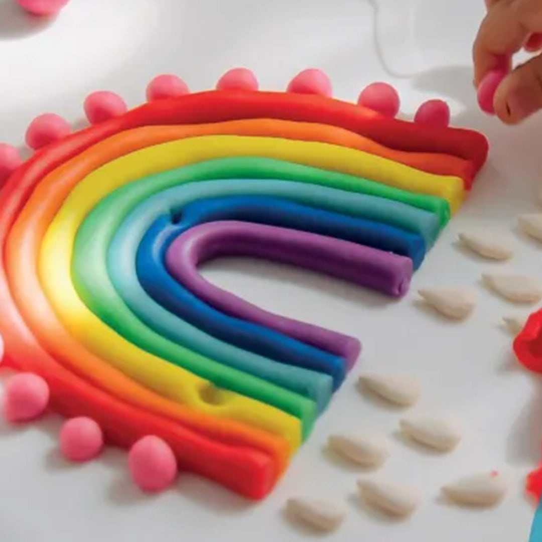 Een regenboog gemaakt van Knetä speelklei in verschillende kleuren, met kleine roze balletjes en witte vormen eromheen.
