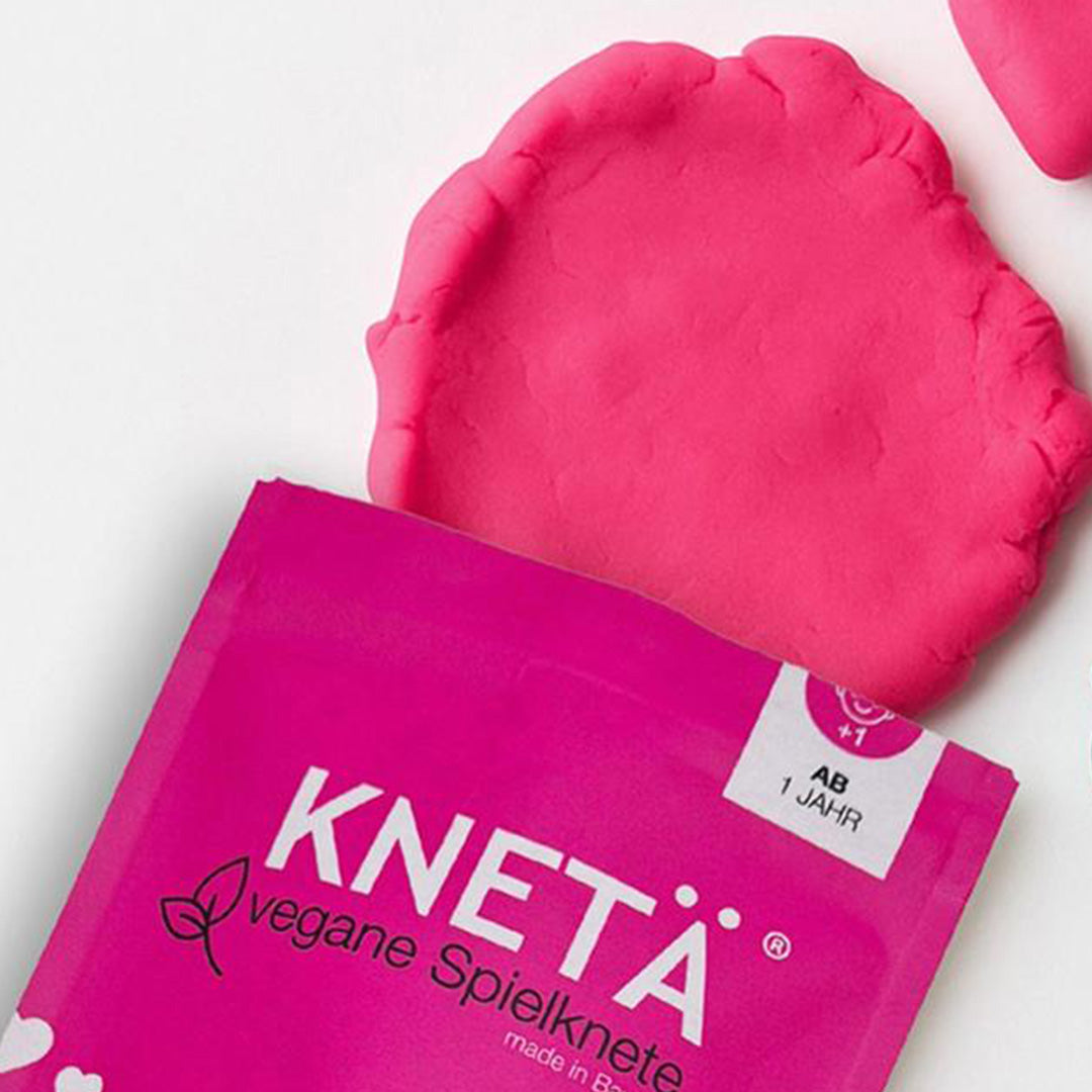 Roze Knetä speelklei uit de verpakking, deels platgedrukt.