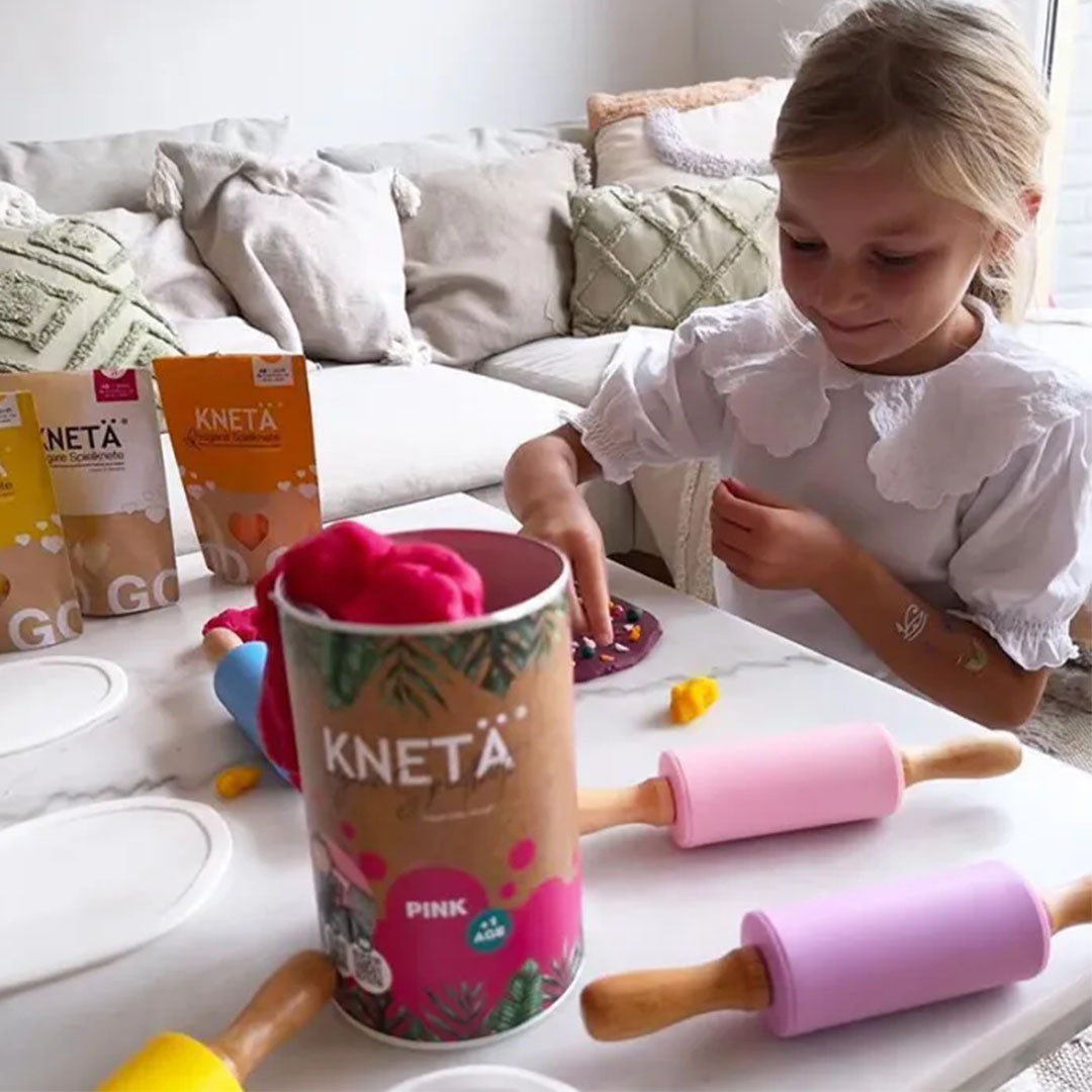Een meisje speelt aan tafel met Knetä speelklei en een roze deegroller.