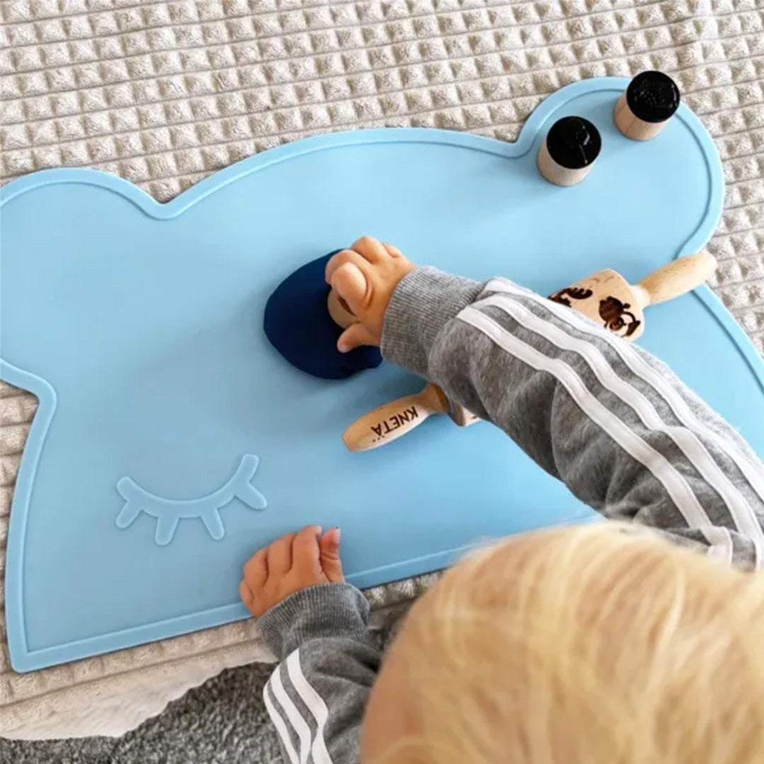 Een kind speelt met Knetä houten stempels en een deegroller op een blauwe siliconen speelmat.