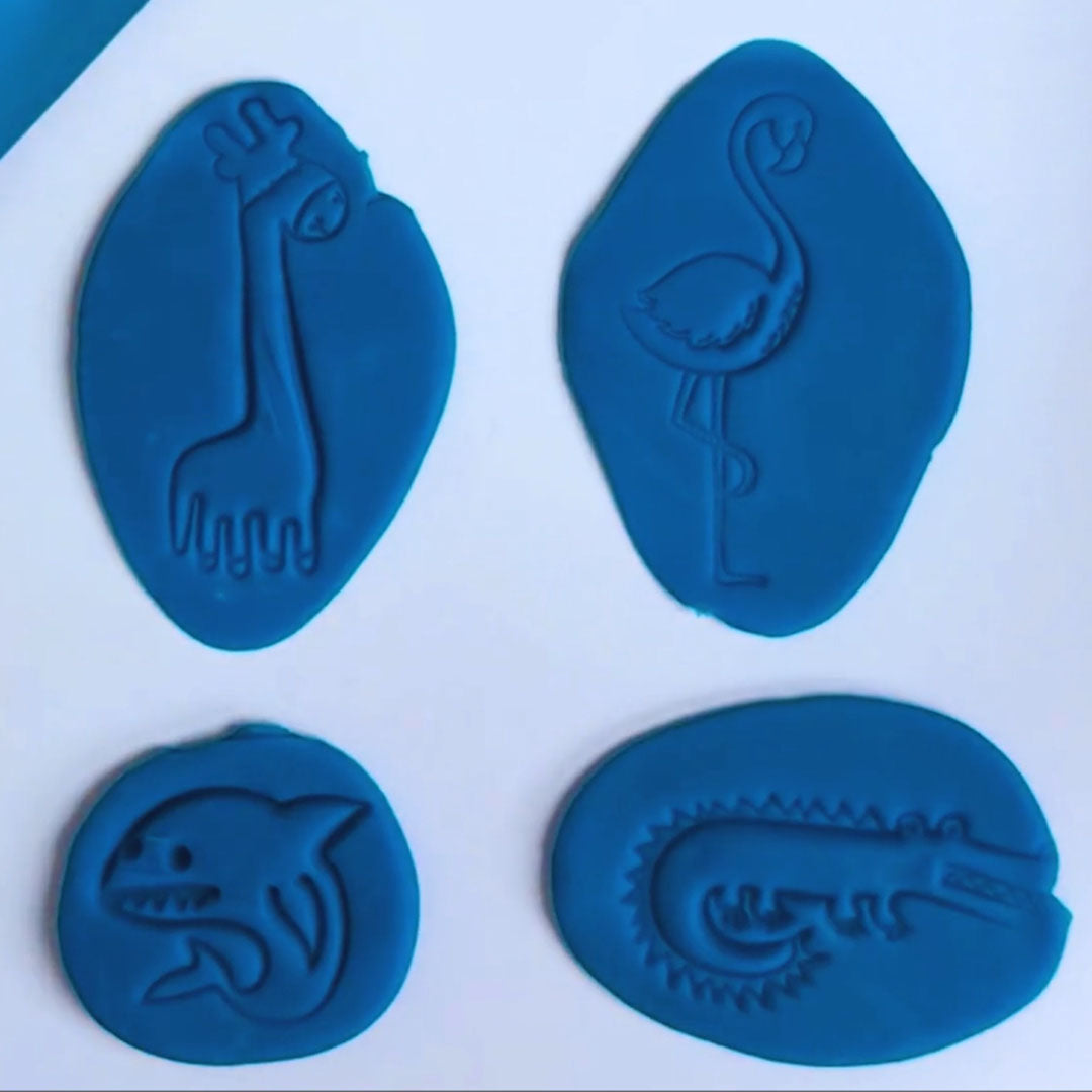 Vier afdrukken van dieren uitsteekvormen, een giraf, flamingo, haai en krokodil, in blauwe klei.