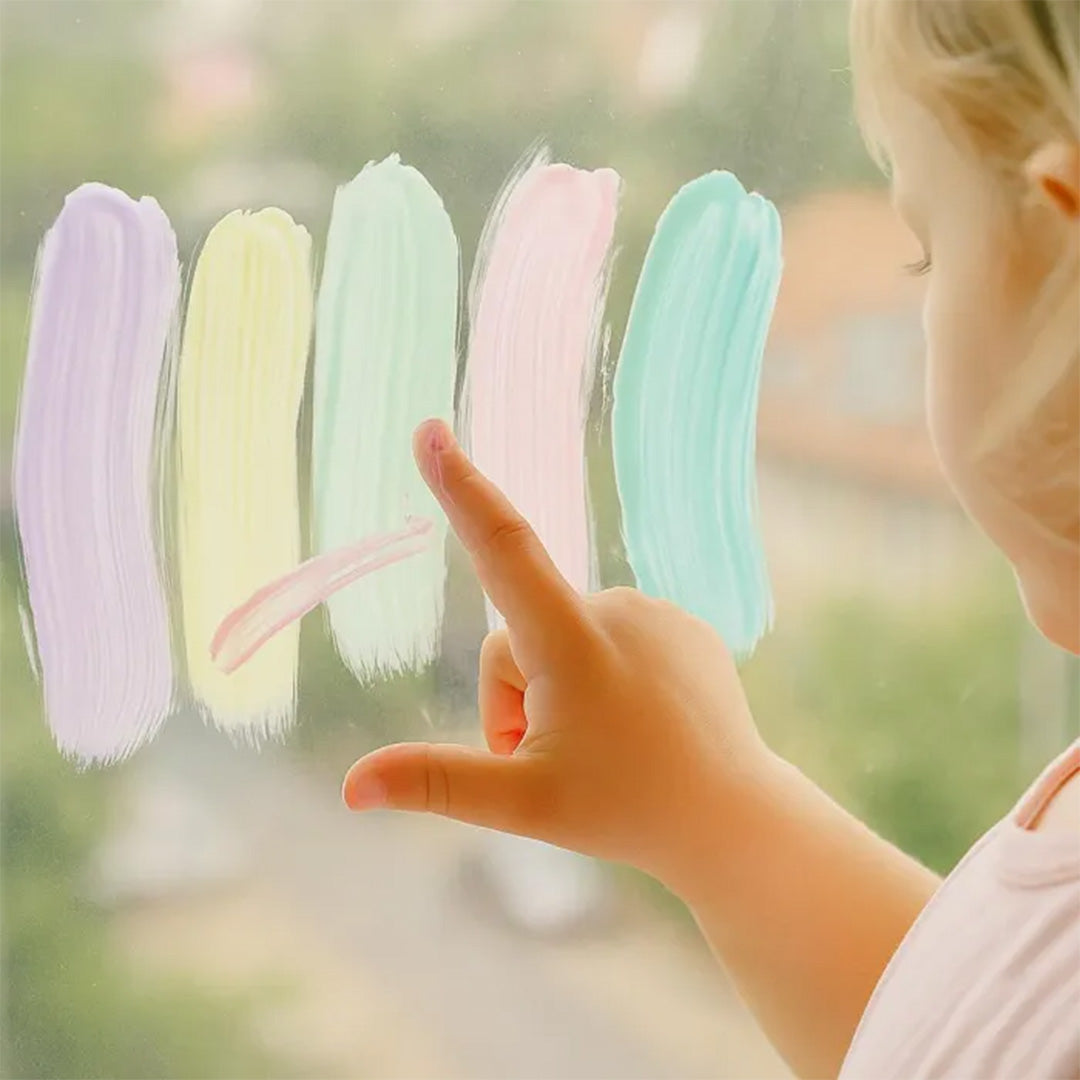 Een kinderhand wijst naar vijf verticale strepen pastelkleurige vingerverf op een raam.