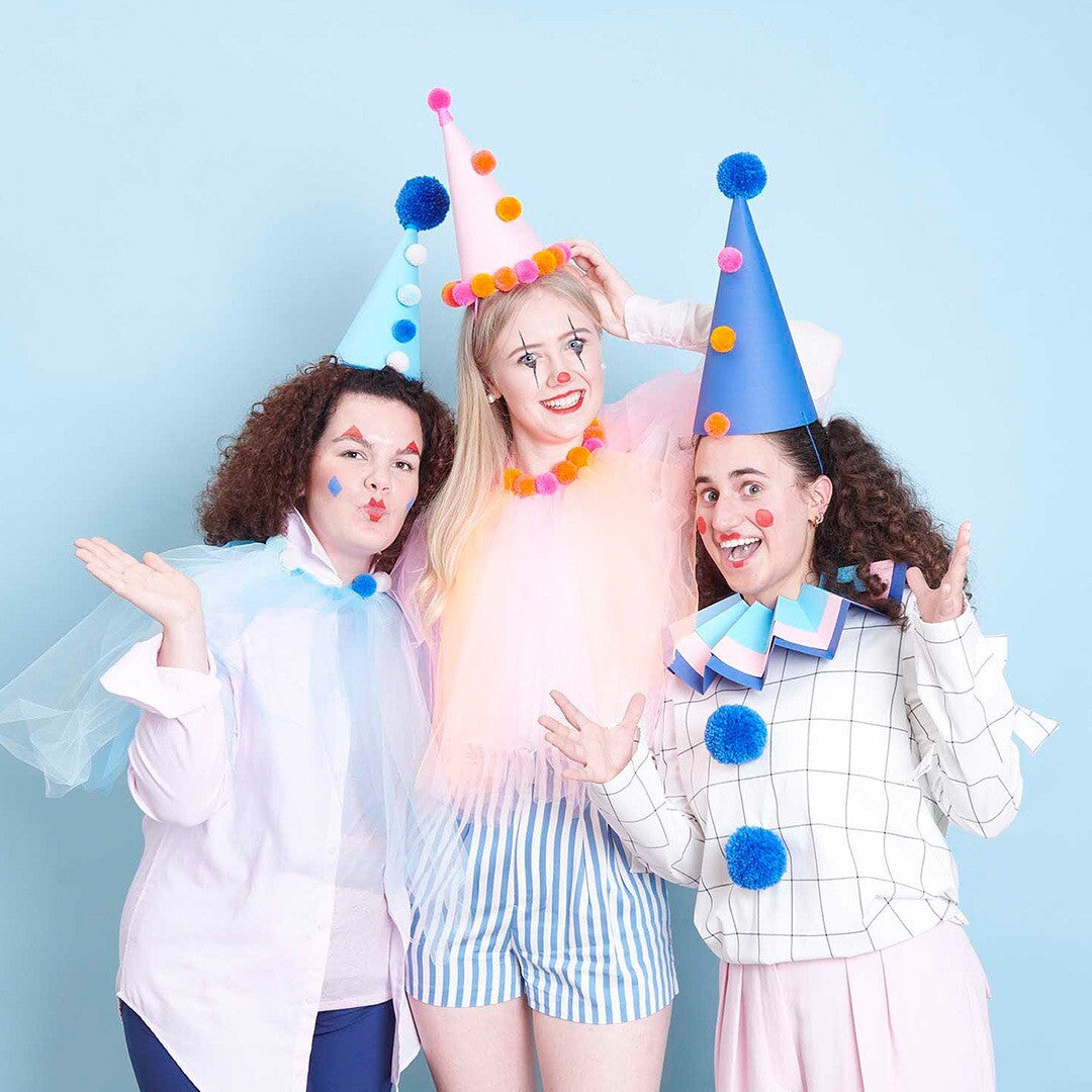 Drie mensen verkleed als clowns met kleurrijke kostuums en puntmutsen.