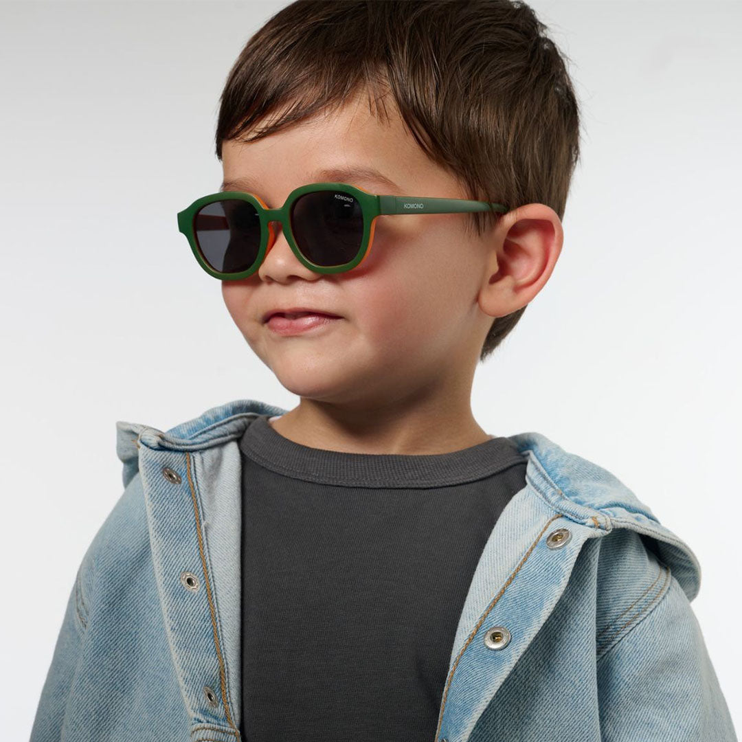 Een jong kind draagt de Komono kinderzonnebril met groen montuur en oranje accenten.