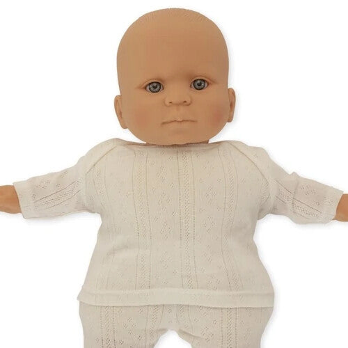 Close-up van de Konges Sløjd babypop Alfie met lichte huid en blauwe ogen, gekleed in een wit gebreid pakje.