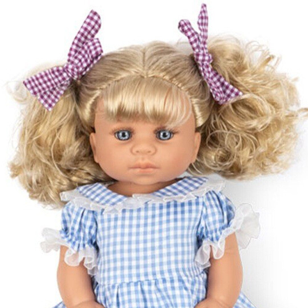 Close-up van Konges Sløjd babypop Delphine met blonde krullen, paarse geruite strikjes en een blauw geruite jurk.