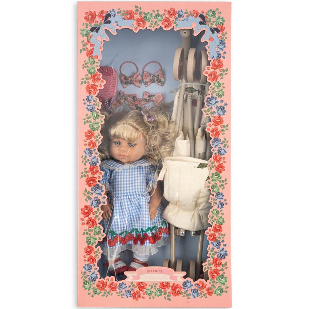De verpakking van de Konges Sløjd babypop Delphine set, een roze doos met bloemenrand en een transparant venster dat de pop en accessoires toont.