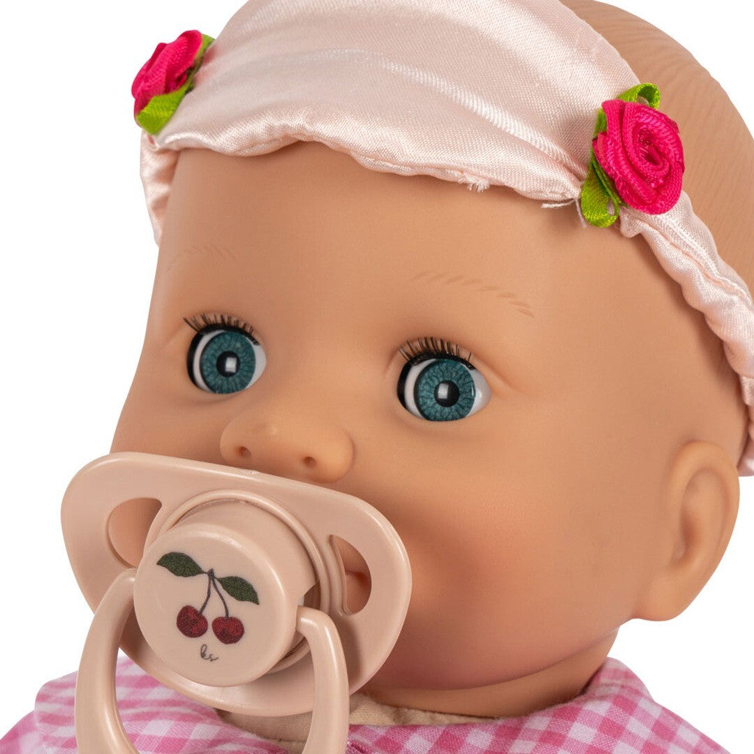 Detail van het gezicht van de babypop met blauwe ogen, roze hoofdband en speen met kersen.