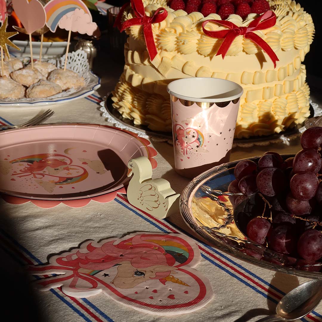 Een feesttafel met een taart, druiven, een roze papieren beker en een bijpassend eenhoornservet.
