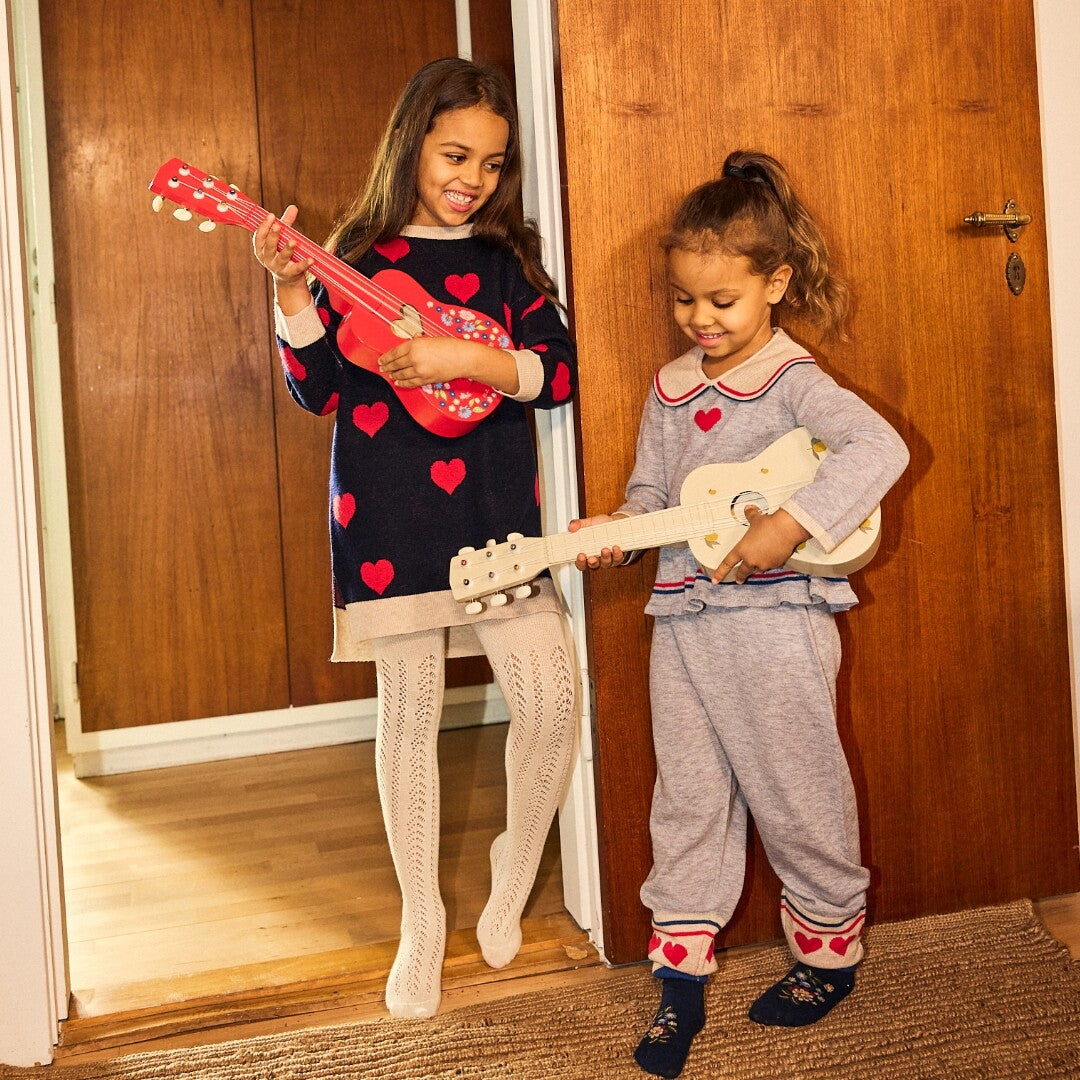 Twee lachende meisjes spelen met een rode en een crèmekleurige speelgoedgitaar.