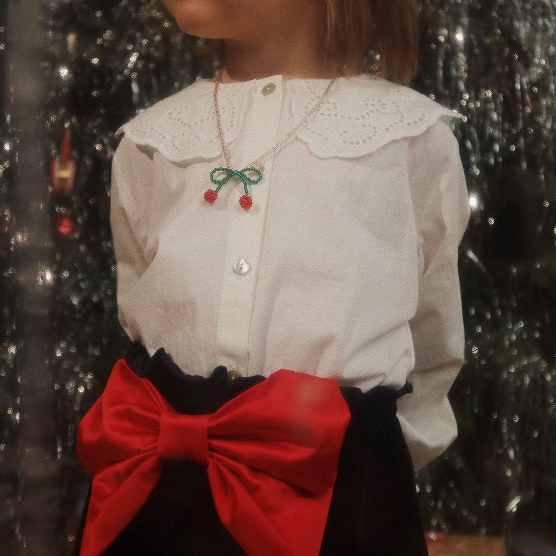 Een kind draagt de Konges Sløjd kersenketting over een witte blouse met kanten kraag.