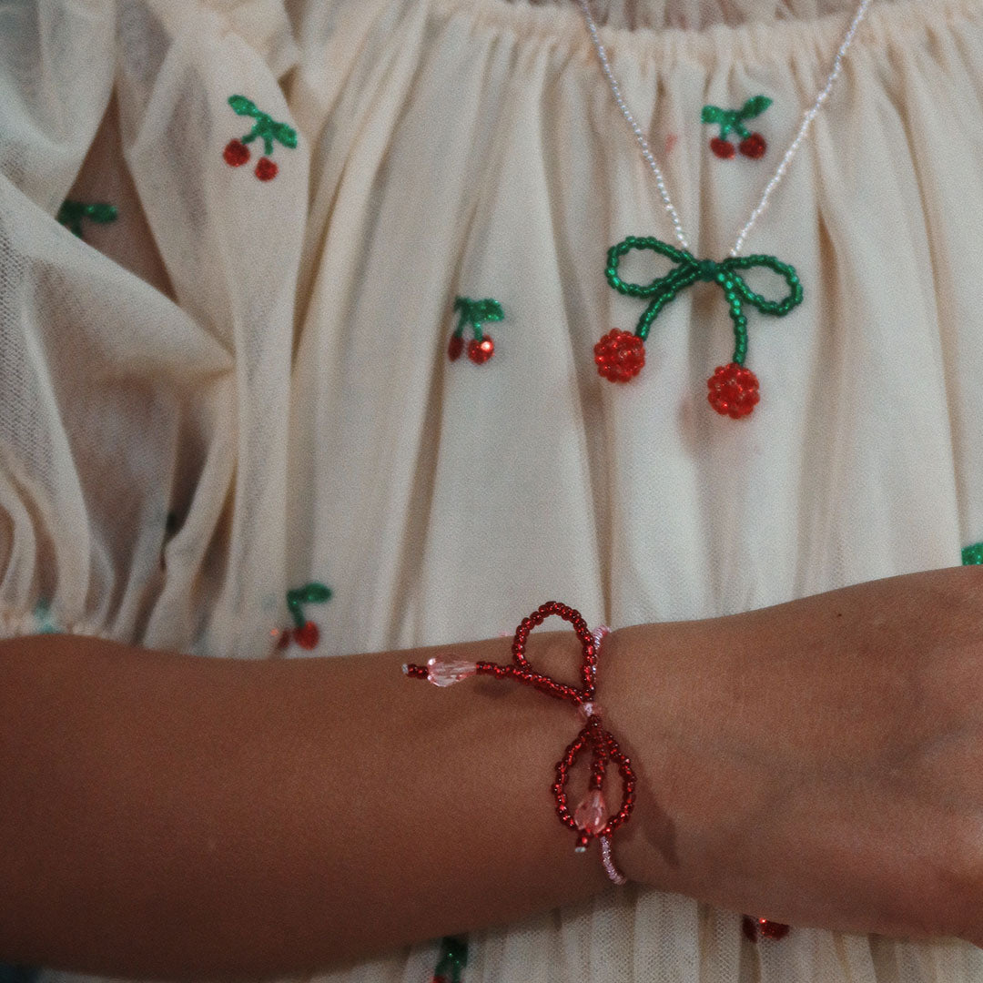Een kind draagt de Konges Sløjd kersenarmband en de bijpassende ketting is zichtbaar op de achtergrond.