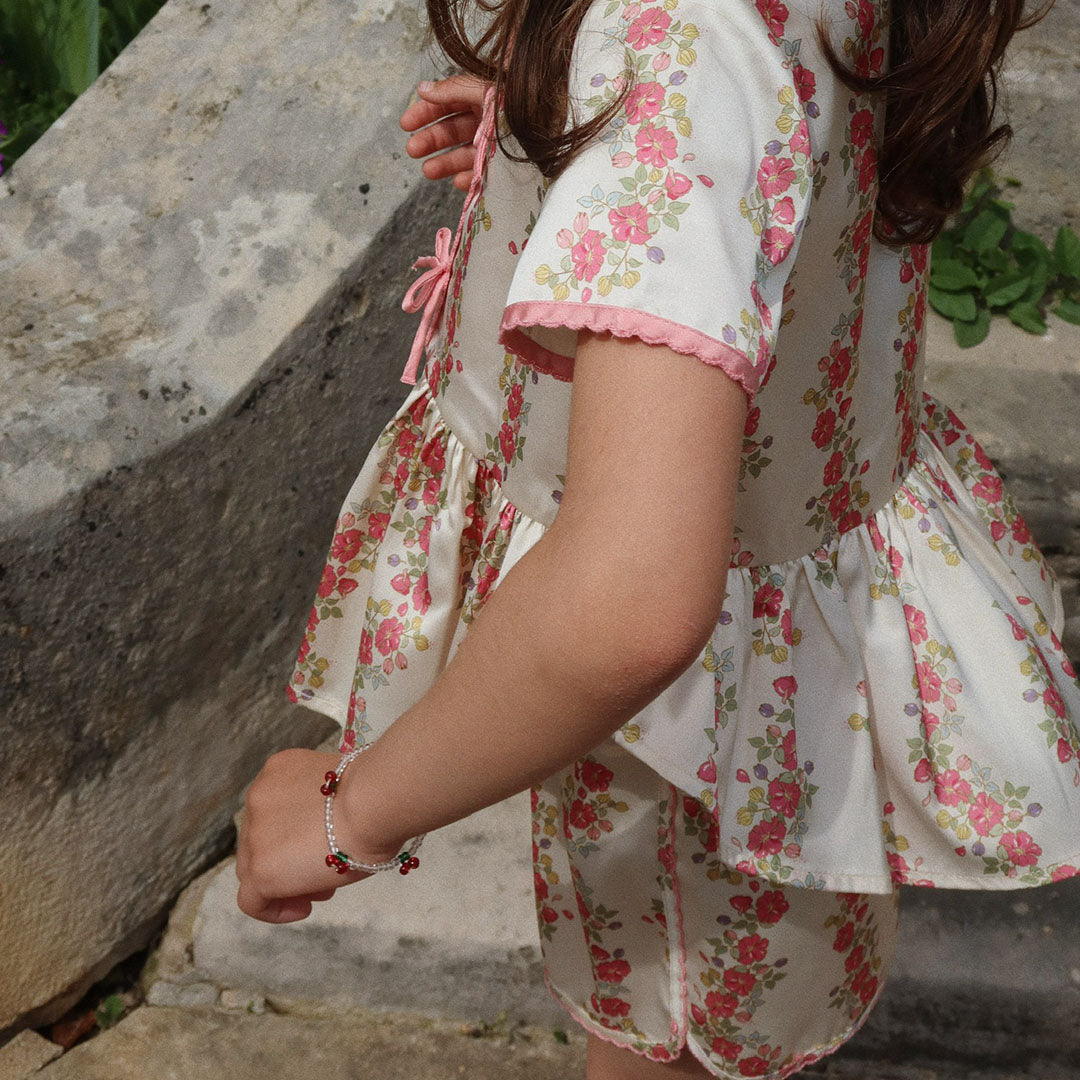 Een kind met bloemenkleding draagt de Konges Sløjd kinderarmband met kersjes om de pols.
