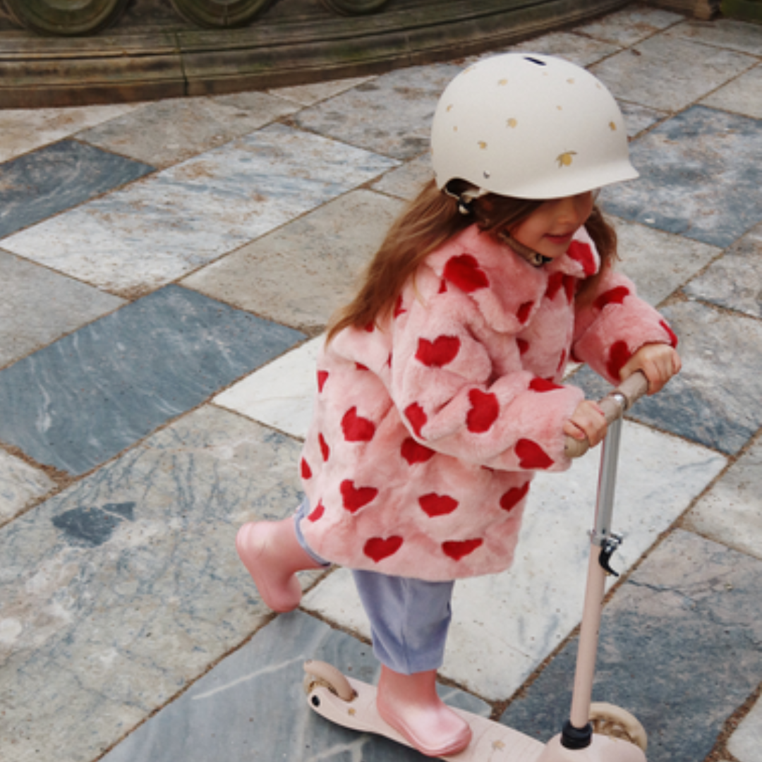 Een meisje met de beige kinderhelm met citroenpatroon rijdt op een scooter.